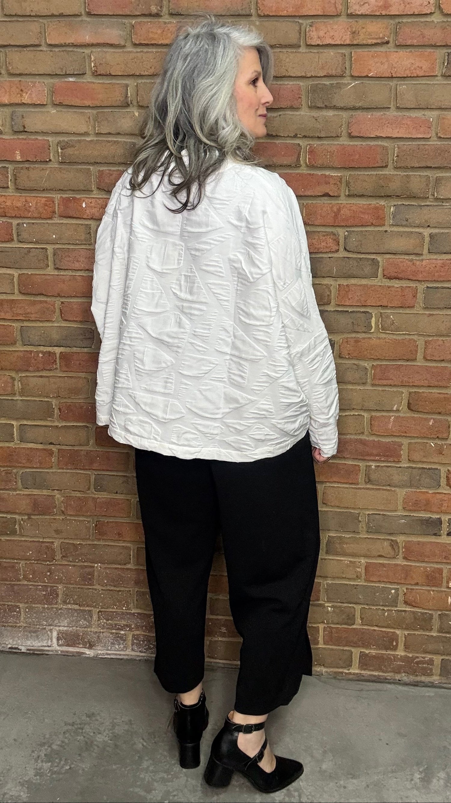 Person wearing a white shirt and black pants against a brick wall