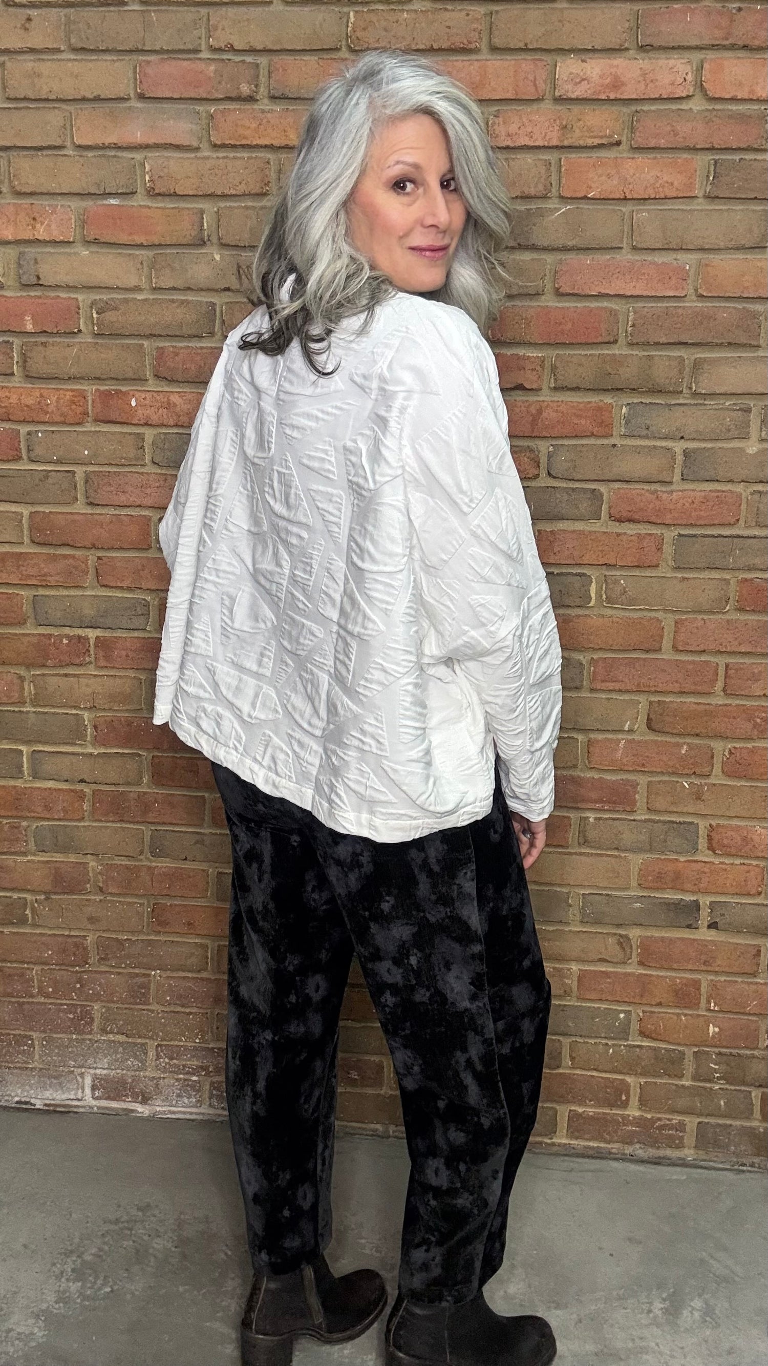 Person wearing a white shirt and black pants standing against a brick wall.