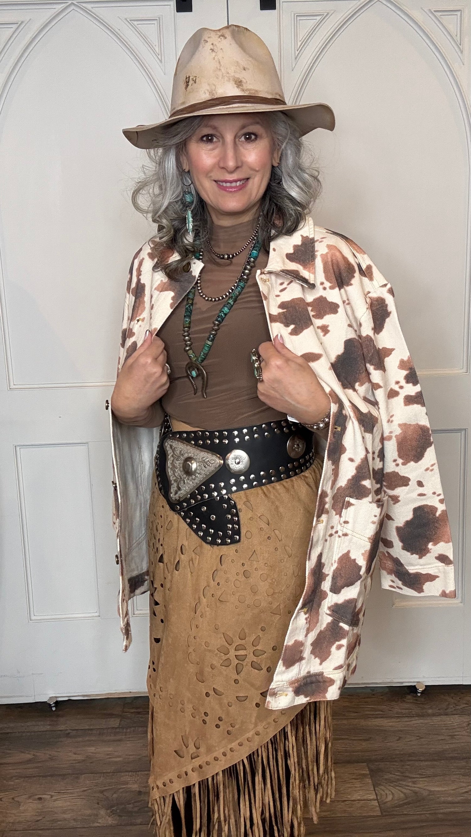 Woman wearing the Cow Print Denim Jacket, the Camel Faux Suede Fringe Skirt, topped the solid Mesh top in Brown and the Wide Triangle Buckle Belt.  Shoes are the Lane Plain Jane Boots, and she is wearing the Pop&
