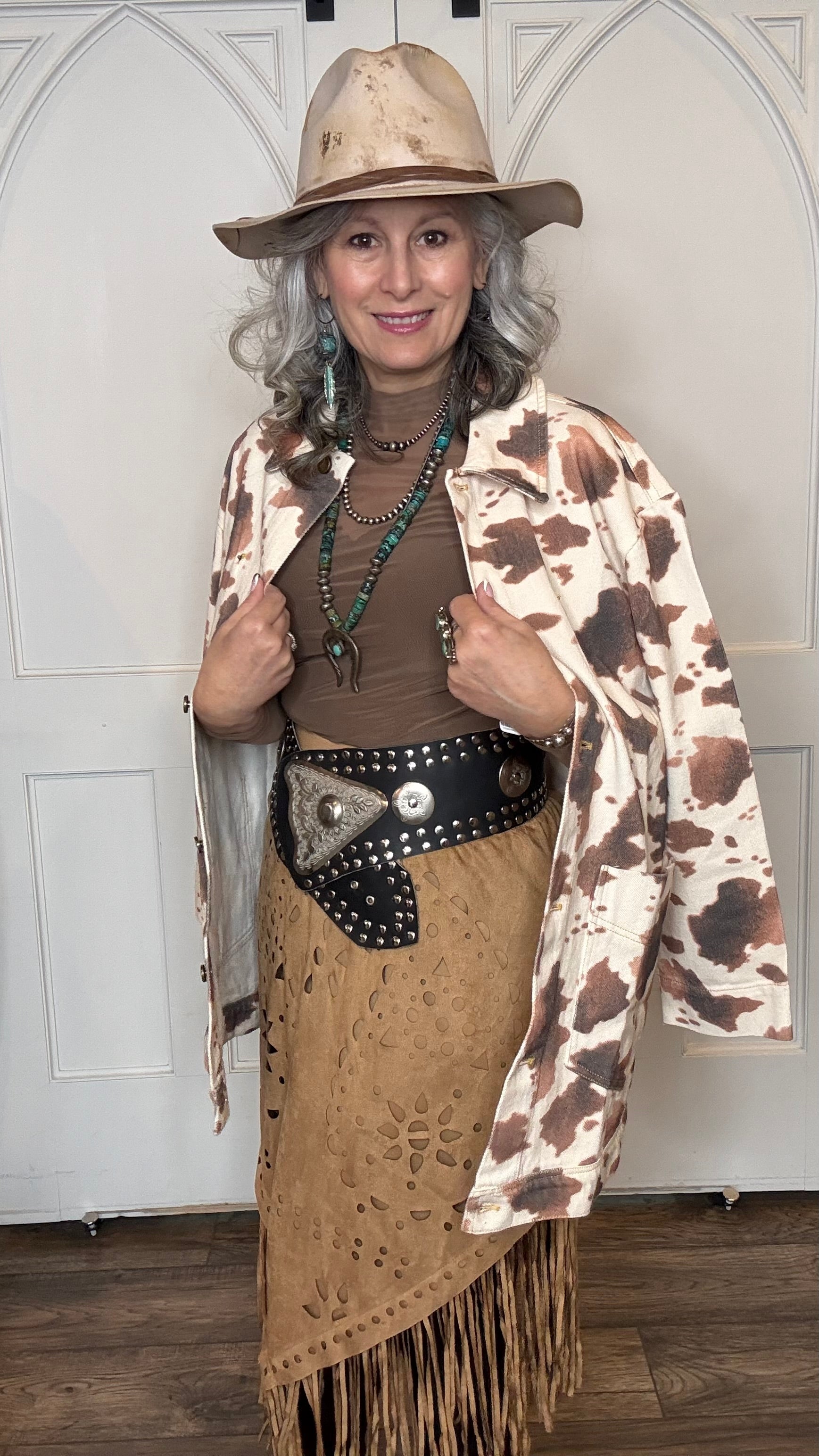 Woman wearing the Cow Print Denim Jacket, the Camel Faux Suede Fringe Skirt, topped the solid Mesh top in Brown and the Wide Triangle Buckle Belt.  Shoes are the Lane Plain Jane Boots, and she is wearing the Pop&