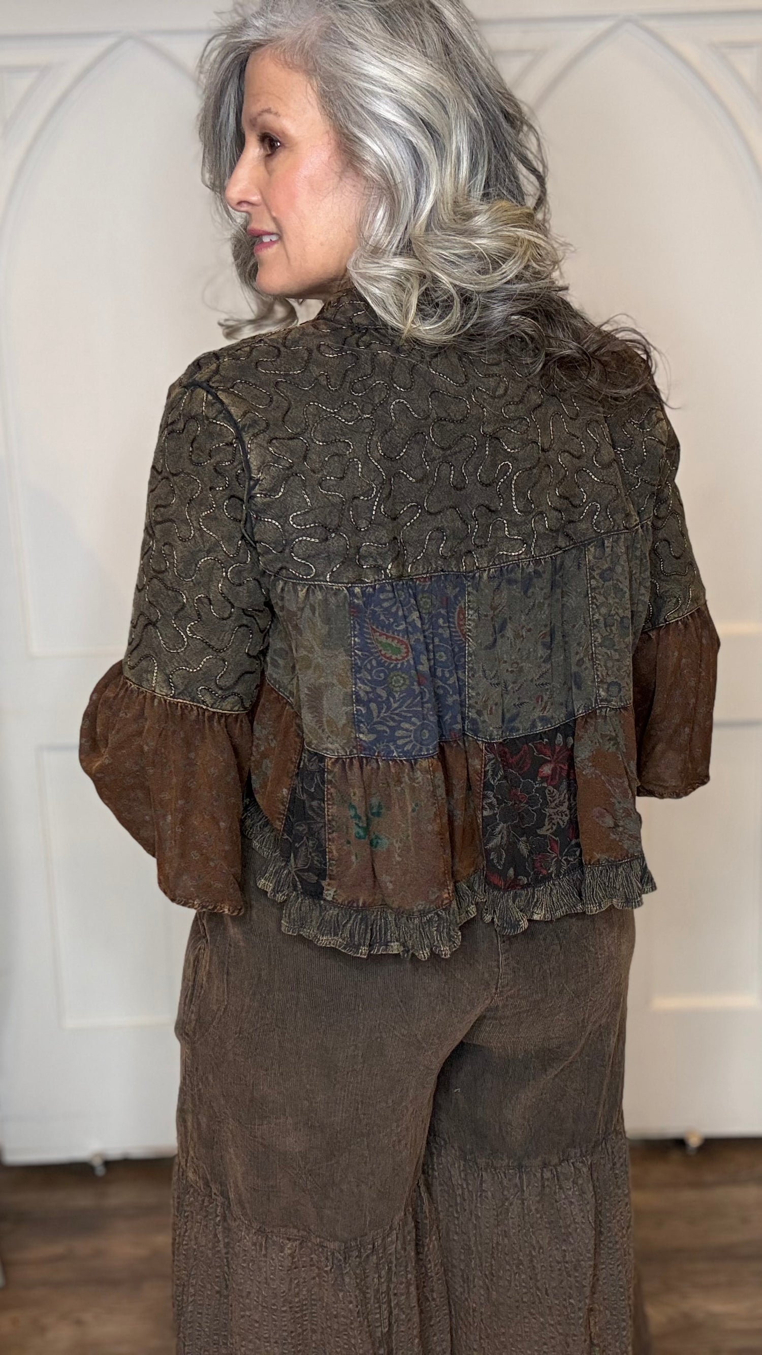 Woman wearing Boho Embroidered Lapel Crop Jacket, beige lace top with Monarch Butterfly Necklace and Amber Boho Chic pants against a white paneled wall.