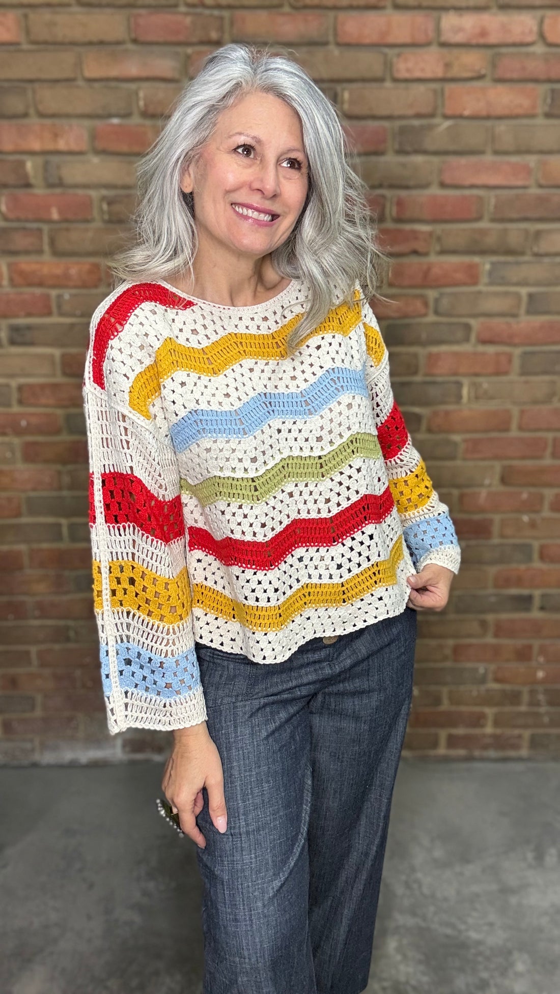 Woman wearing the Sunshine 3/4 Sleeve Crochet Top, a colorful crochet sweater in front of a brick wall.