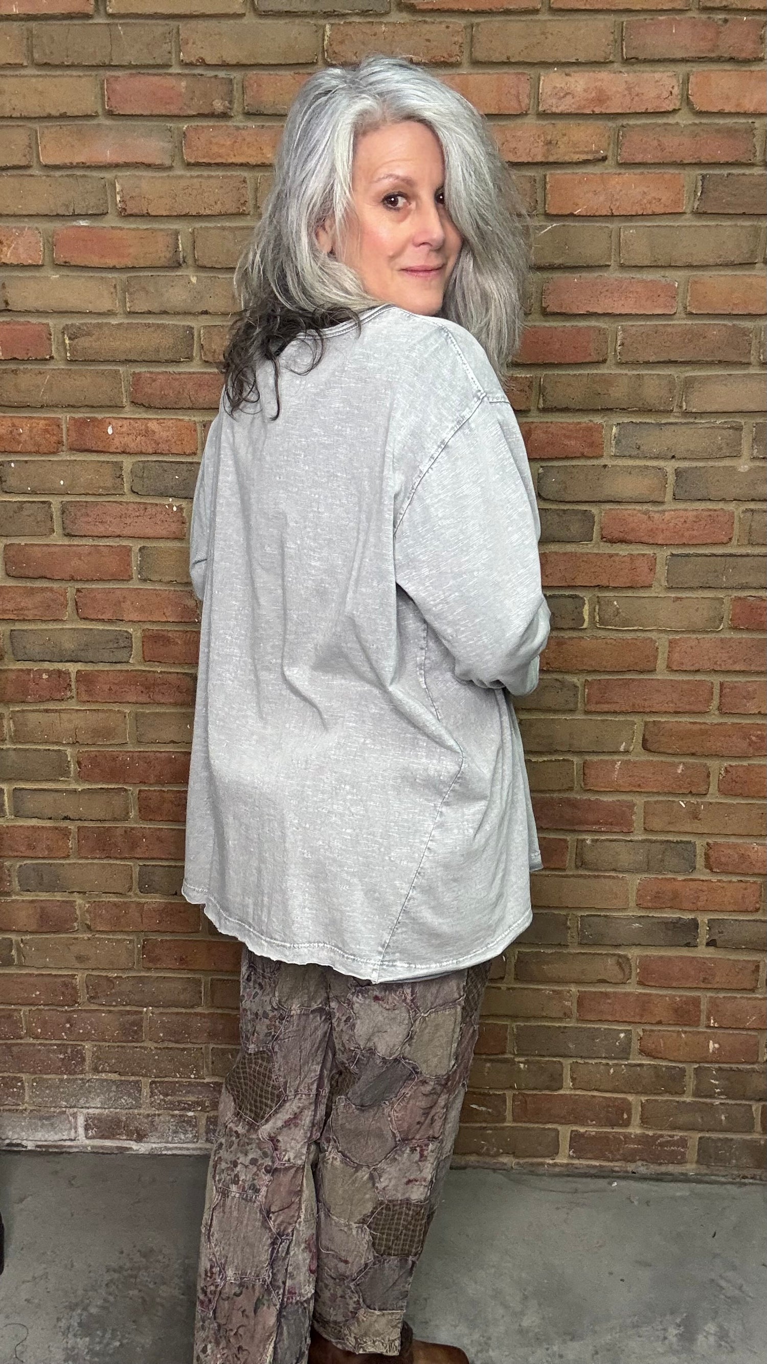 Person wearing a light-colored shirt and patterned pants leaning against a brick wall.