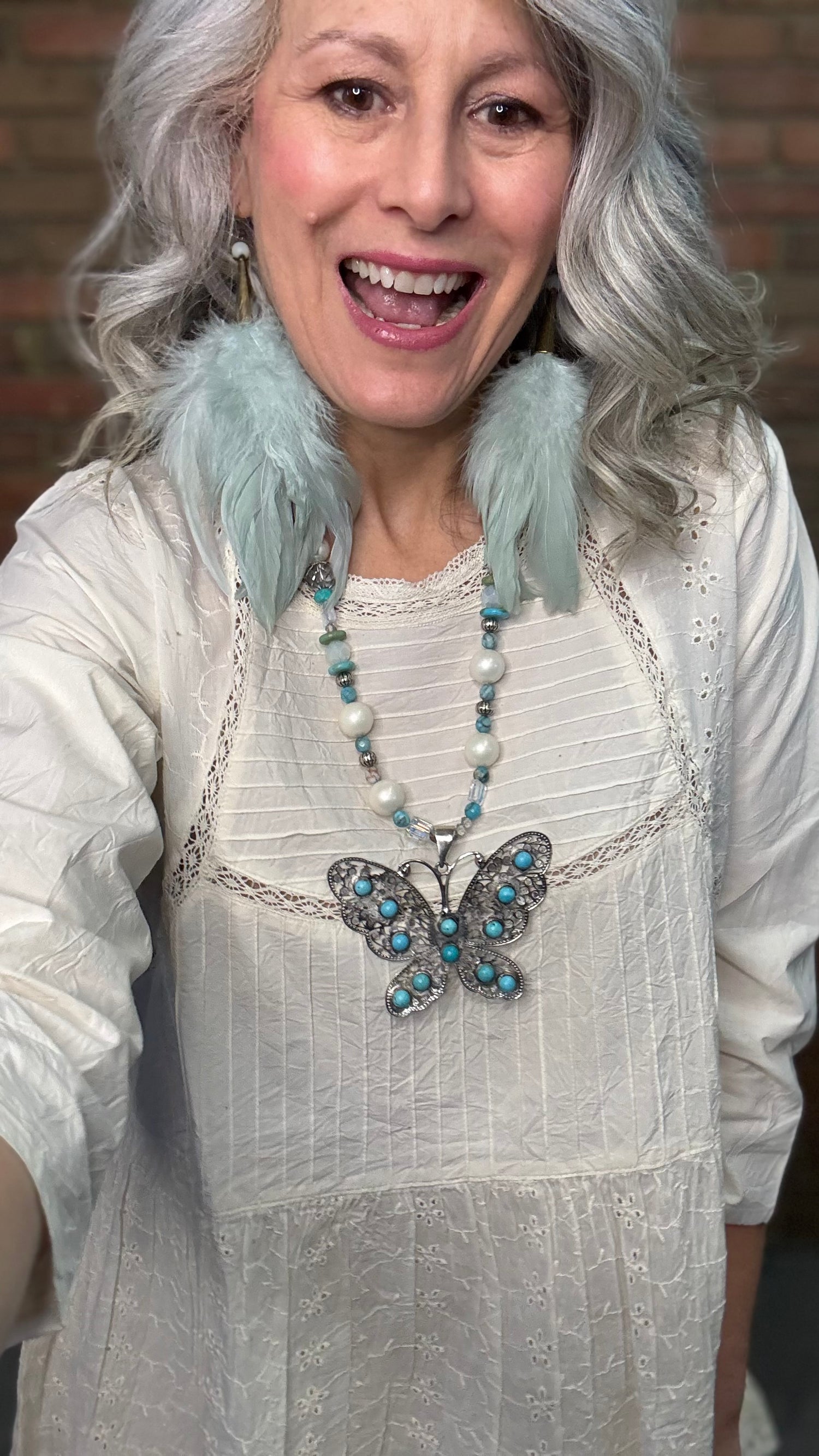Woman wearing Silver Filigree Butterfly Necklace with turquoise stones and sage feather earrings.