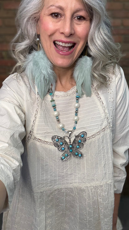 Woman wearing Silver Filigree Butterfly Necklace with turquoise stones and sage feather earrings.