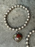 Silver beaded bracelet with a red stone charm on a gray surface