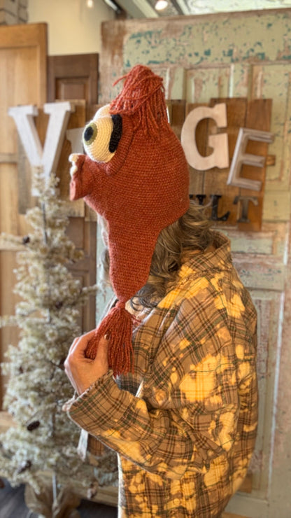 Person wearing a knitted animal hat with a plaid coat in a rustic indoor setting.
