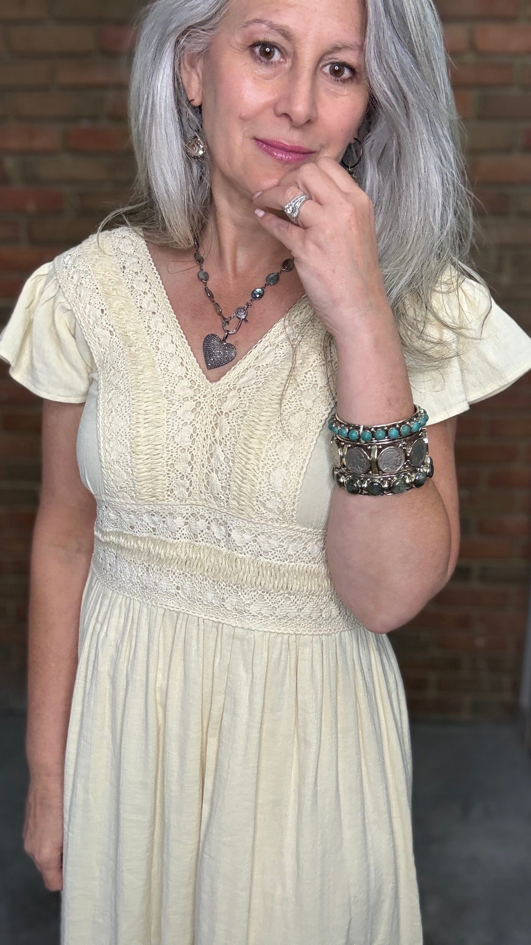 Woman in the Vina Cotton Lace Dress in Ivory standing against a brick wall