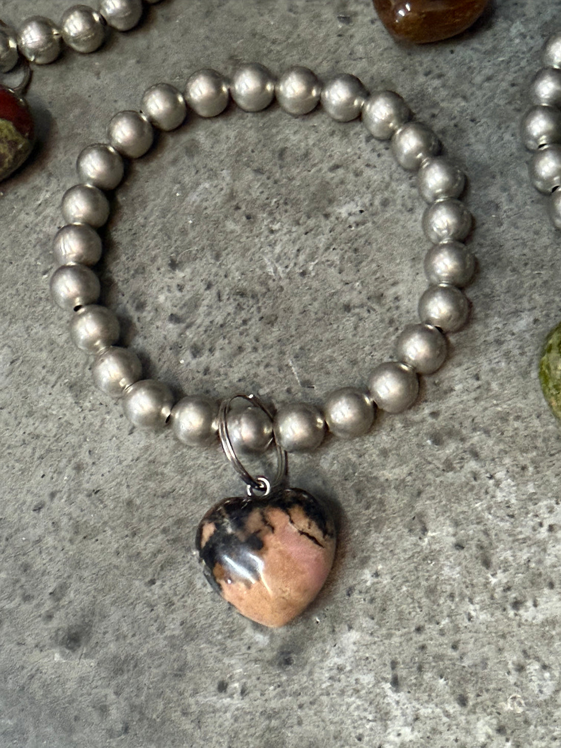 Silver beaded bracelet with a heart-shaped stone charm on a concrete surface