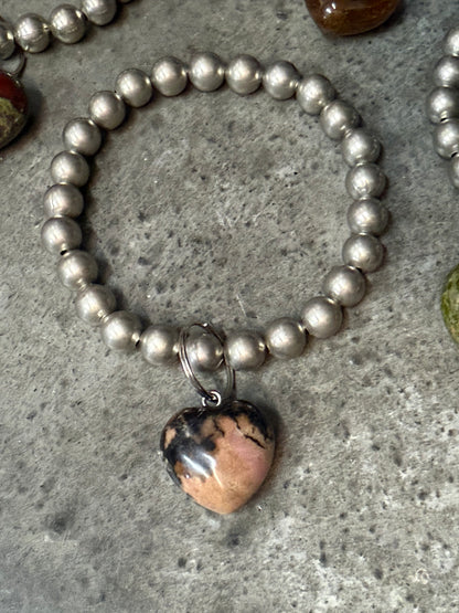 Silver beaded bracelet with a heart-shaped stone charm on a concrete surface