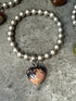 Silver beaded bracelet with a heart-shaped stone charm on a concrete surface