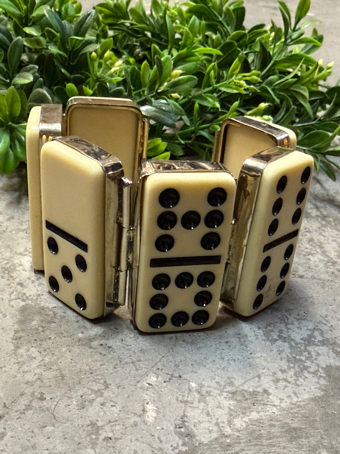 Ivory Dominos forming a bracelet on a textured surface with greenery