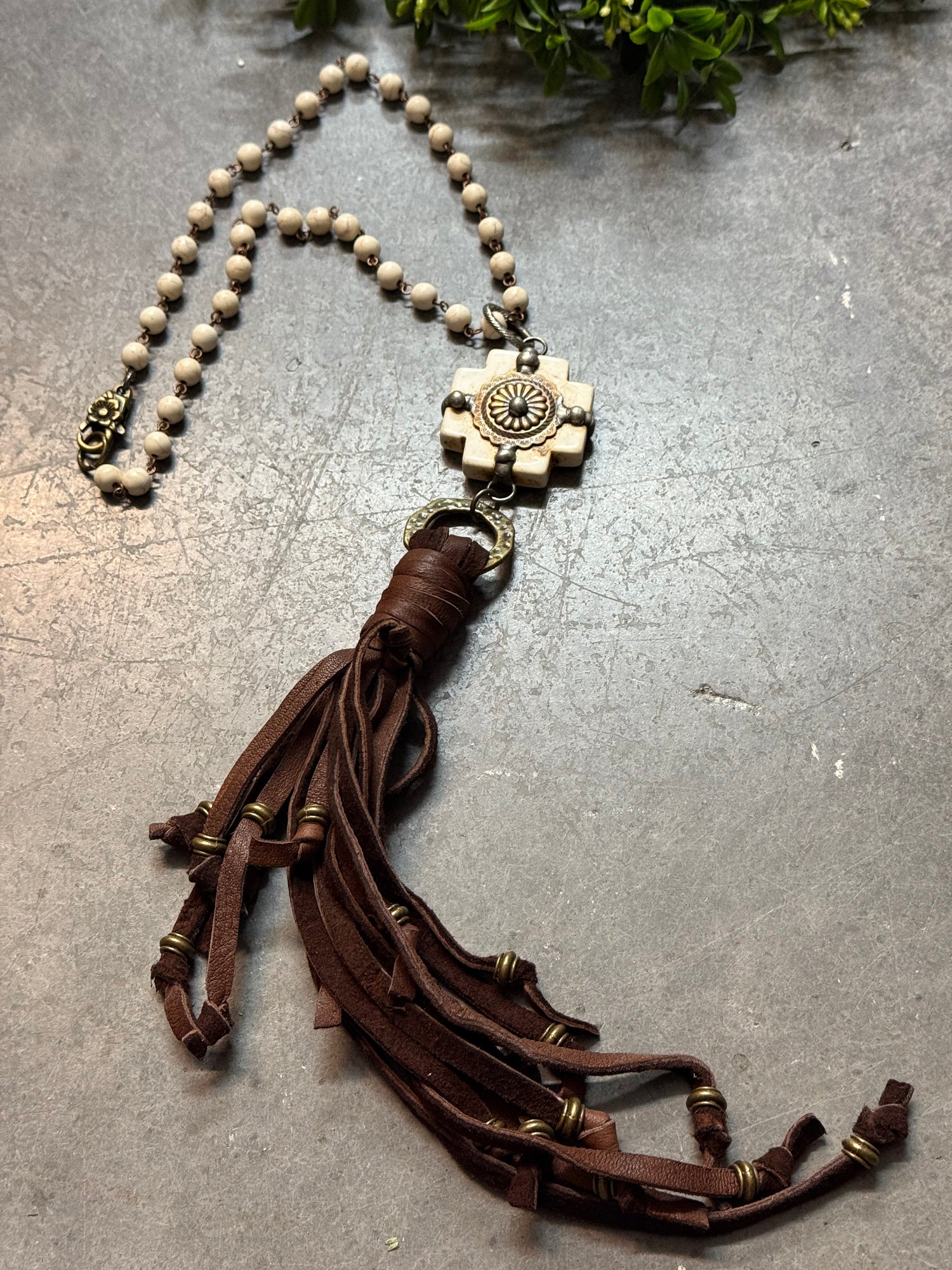 Necklace with brown leather tassel and beige bead chain on a textured surface