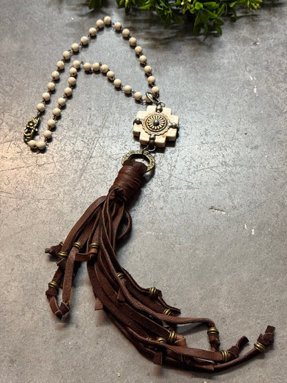 Necklace with brown leather tassel and beige bead chain on a textured surface