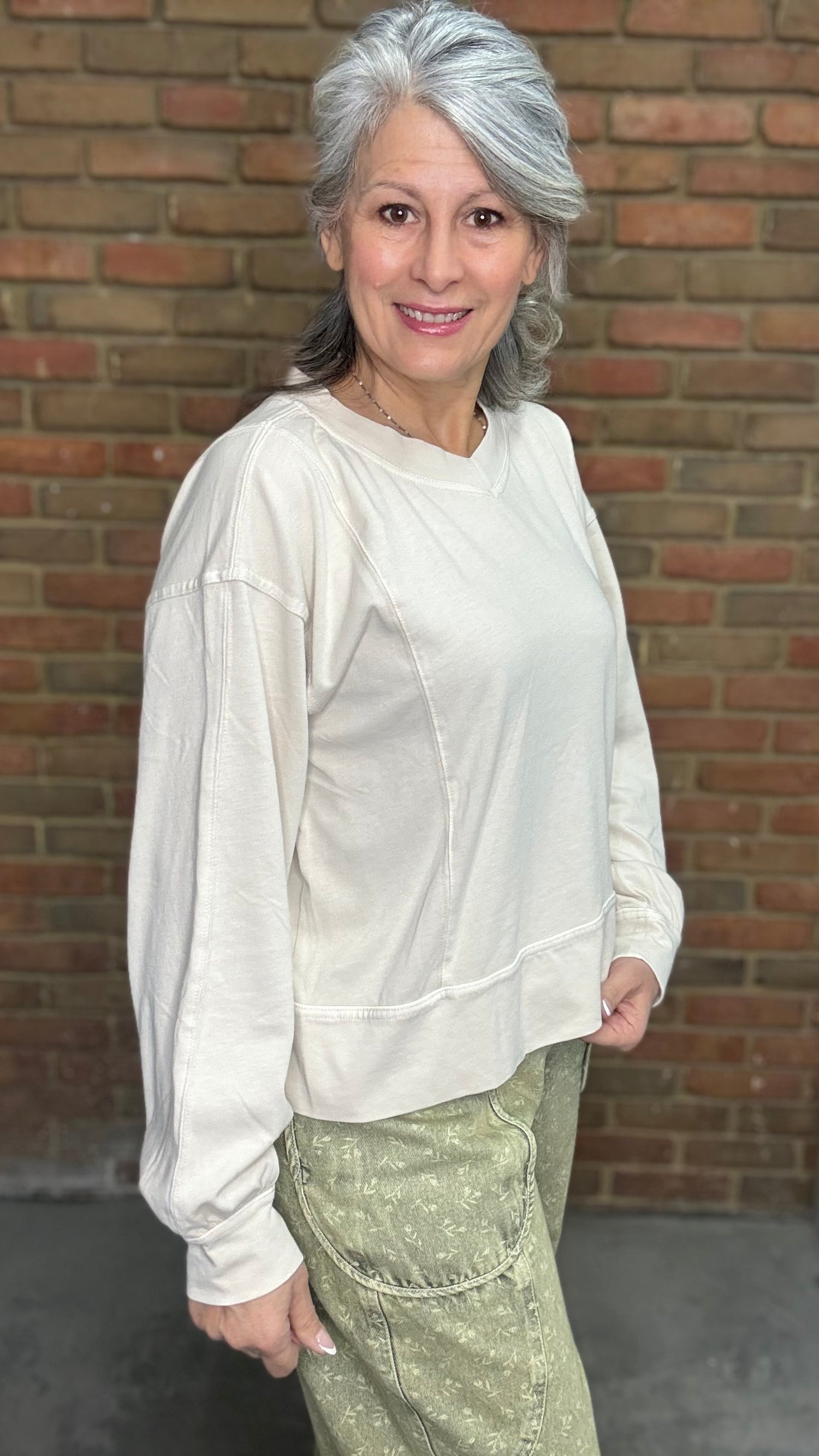 Woman standing against a brick wall wearing the Taupe Long Sleeve Top and Floral Printed Barrel Pants.