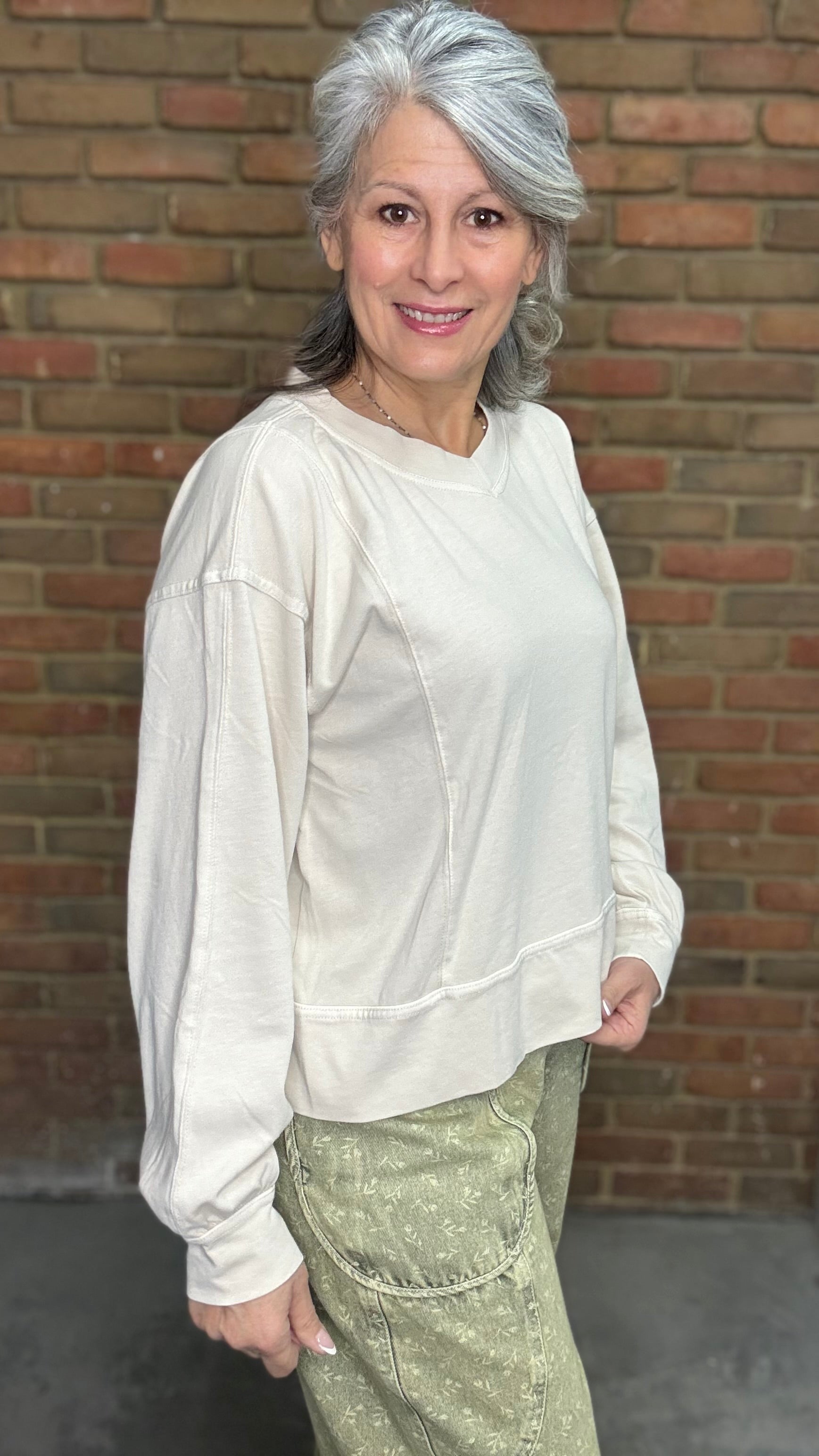 Woman standing against a brick wall wearing the Taupe Long Sleeve Top and Floral Printed Barrel Pants.