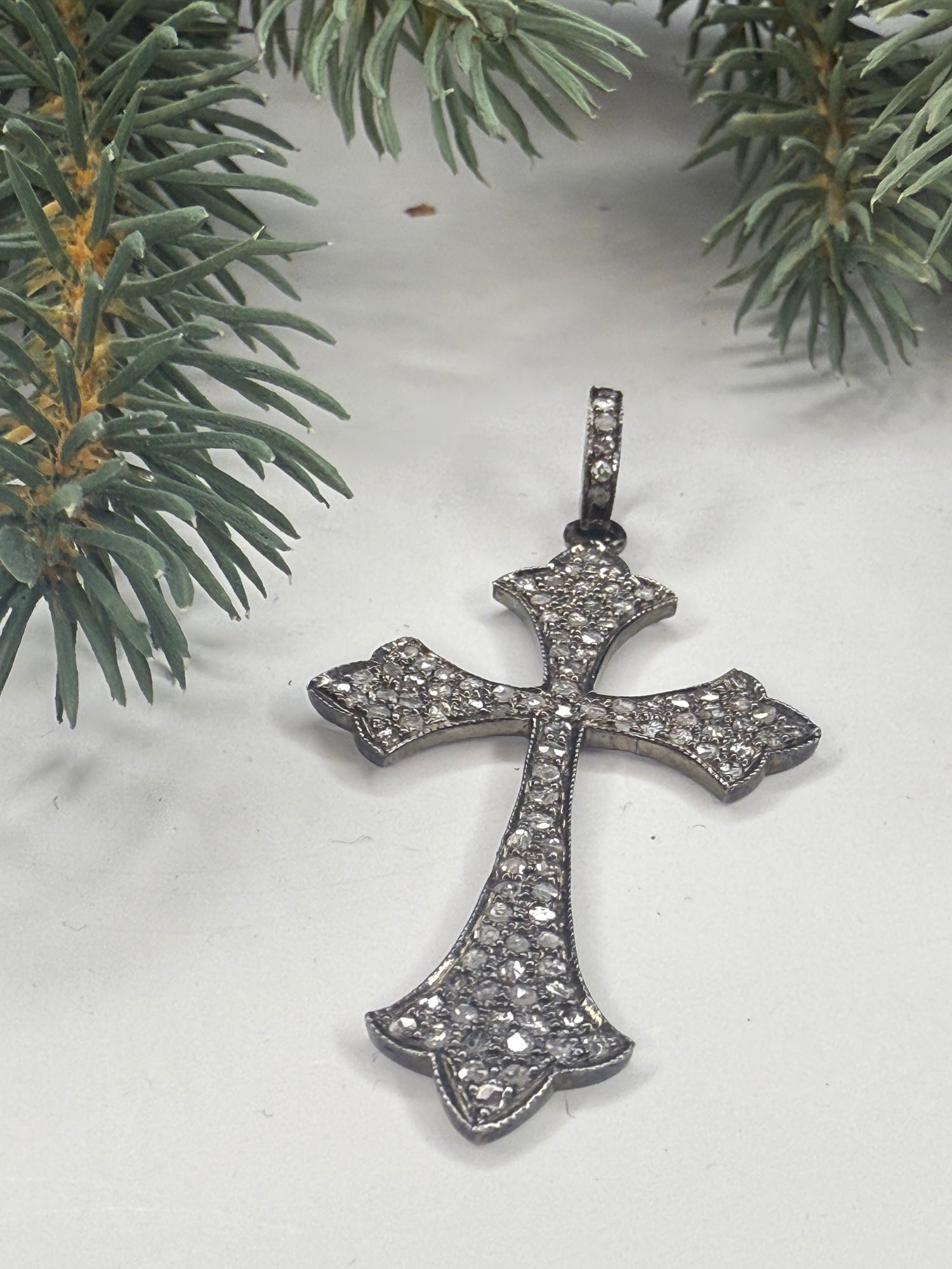 Silver cross pendant with pave diamonds on a white background with greenery