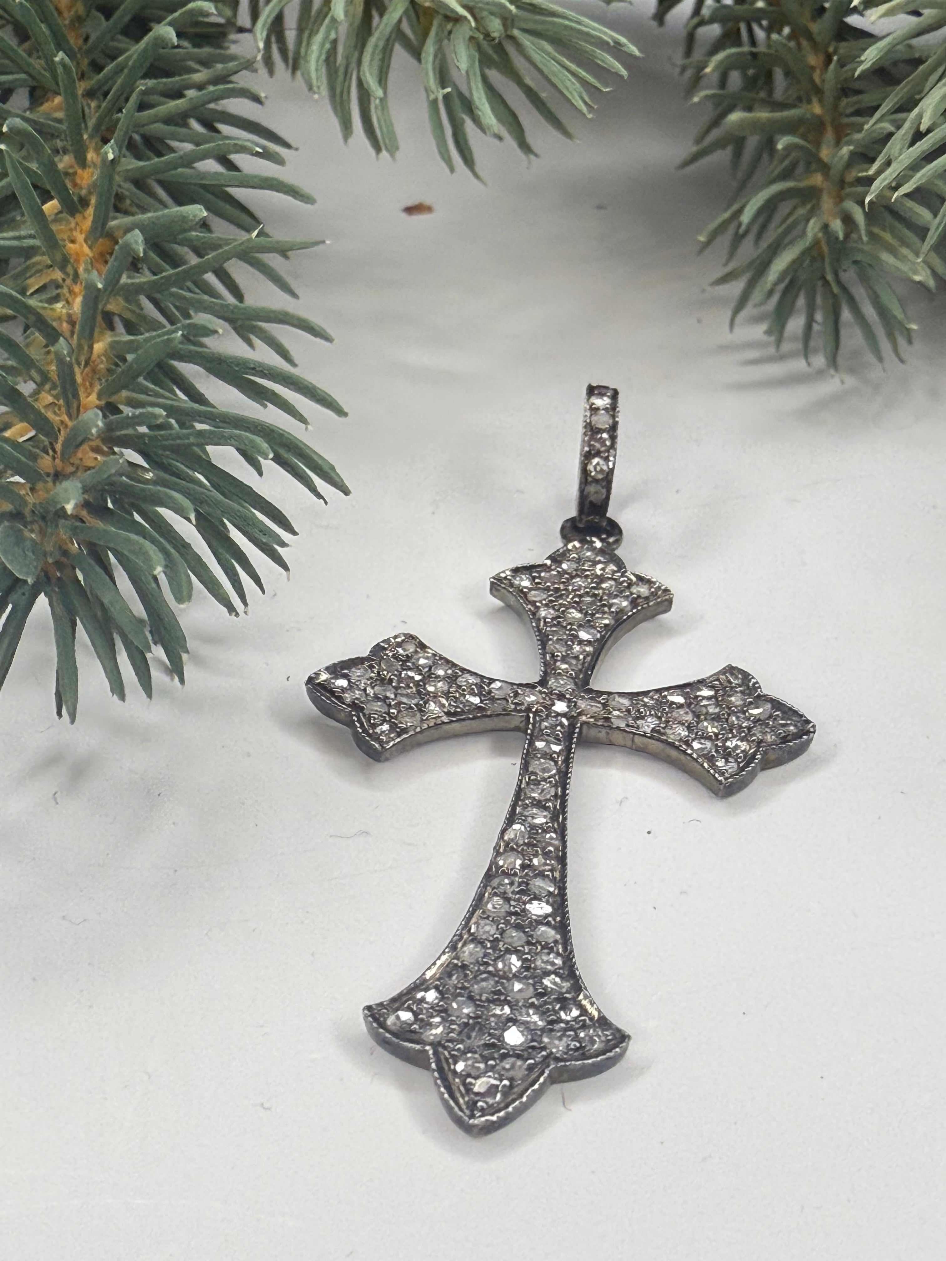 Silver cross pendant with pave diamonds on a white background with greenery