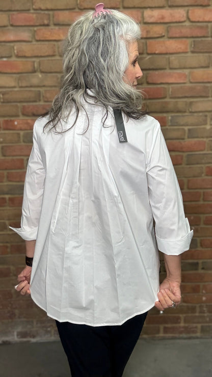 Person wearing a white shirt with a visible brand logo against a brick wall.