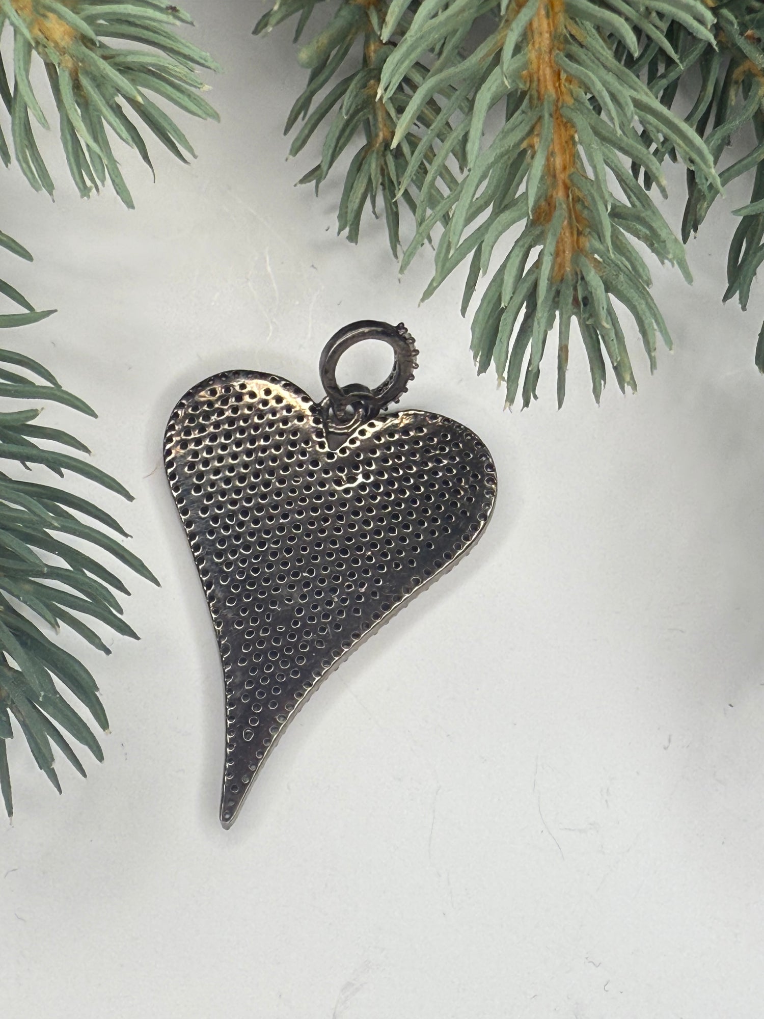 Back of heart-shaped pendant on a light background with greenery