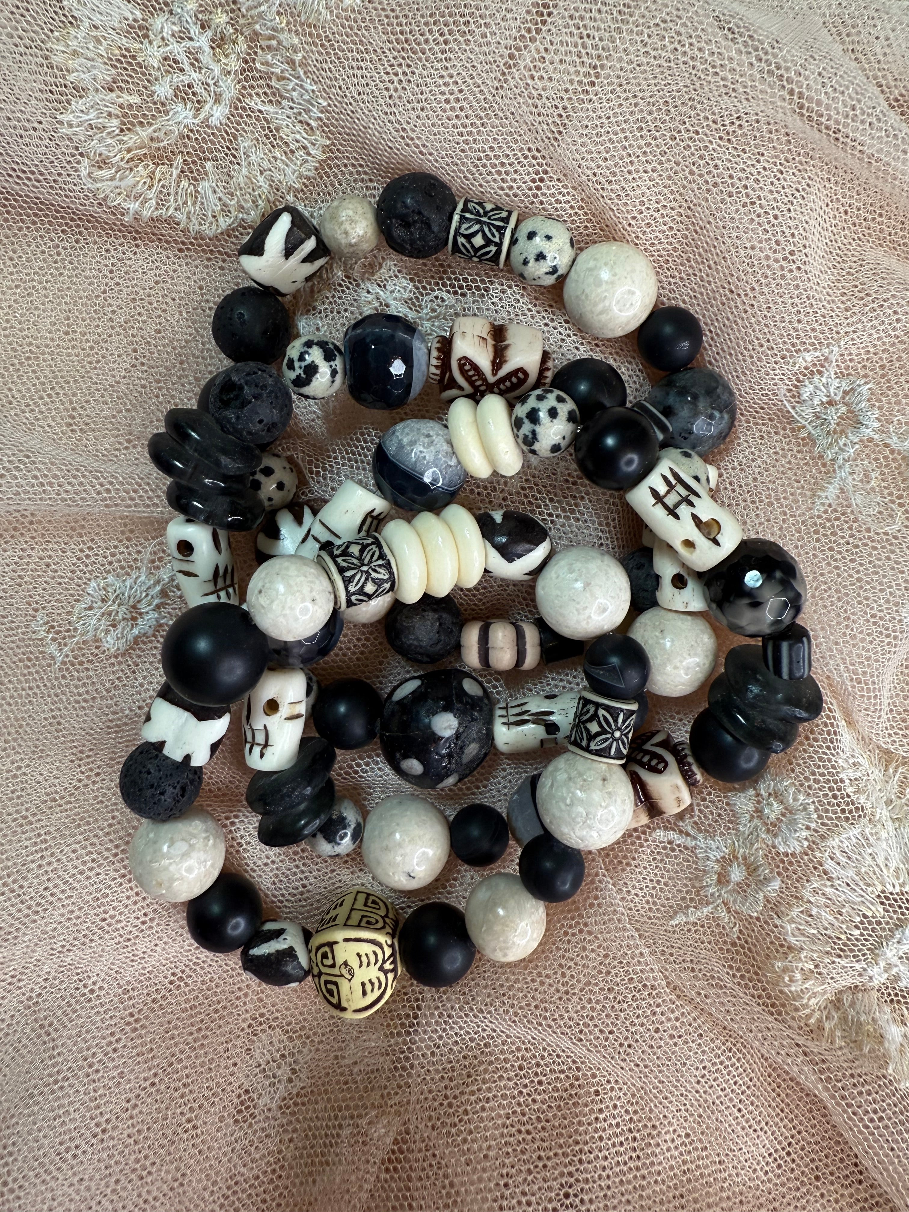 Stack of black, white, and gray beaded bracelets on a textured beige fabric background