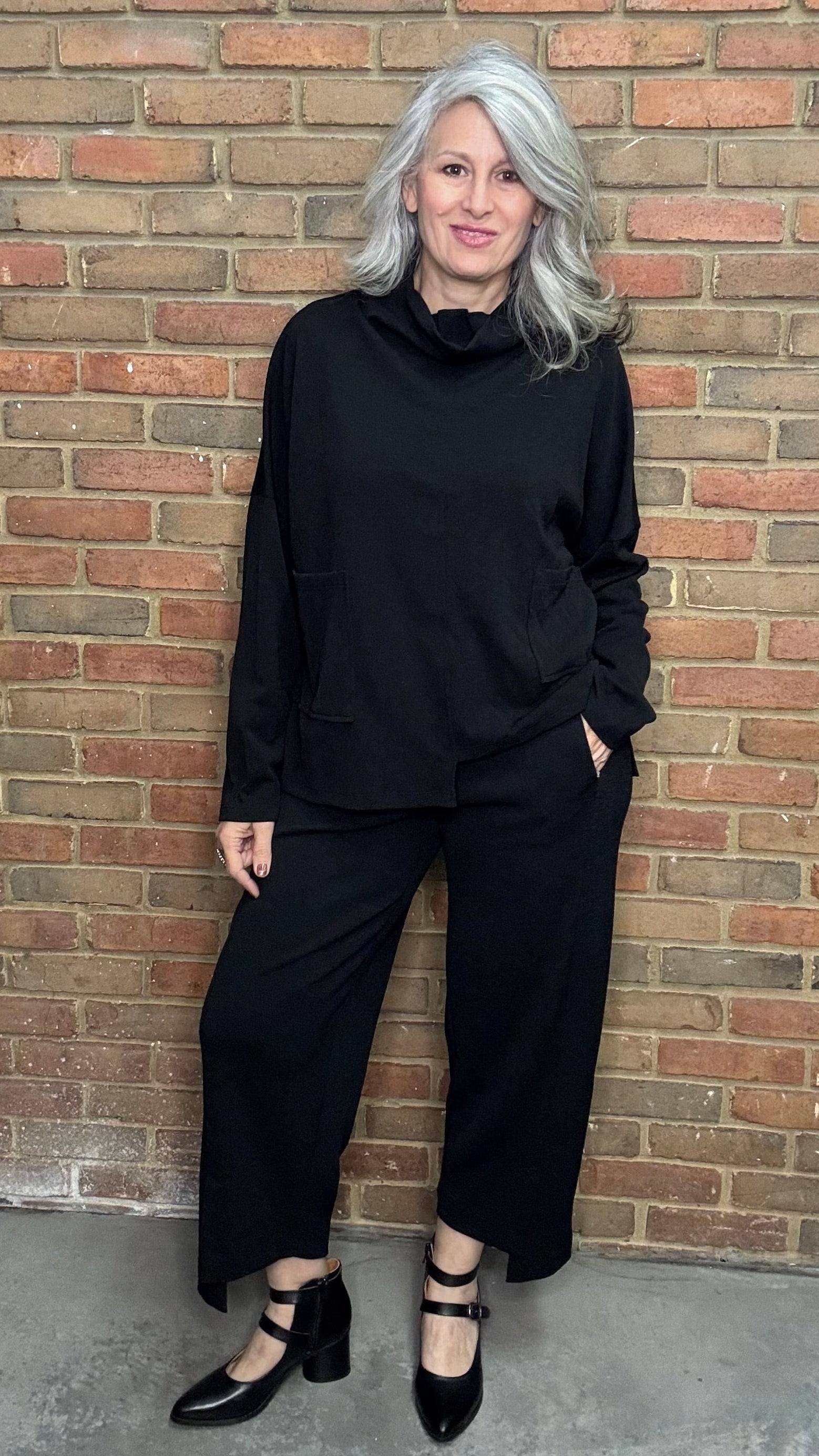 Woman in black outfit standing against a brick wall