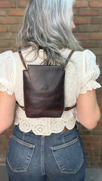 Woman holding a Backpack style leather Handbag with a brick wall in background.