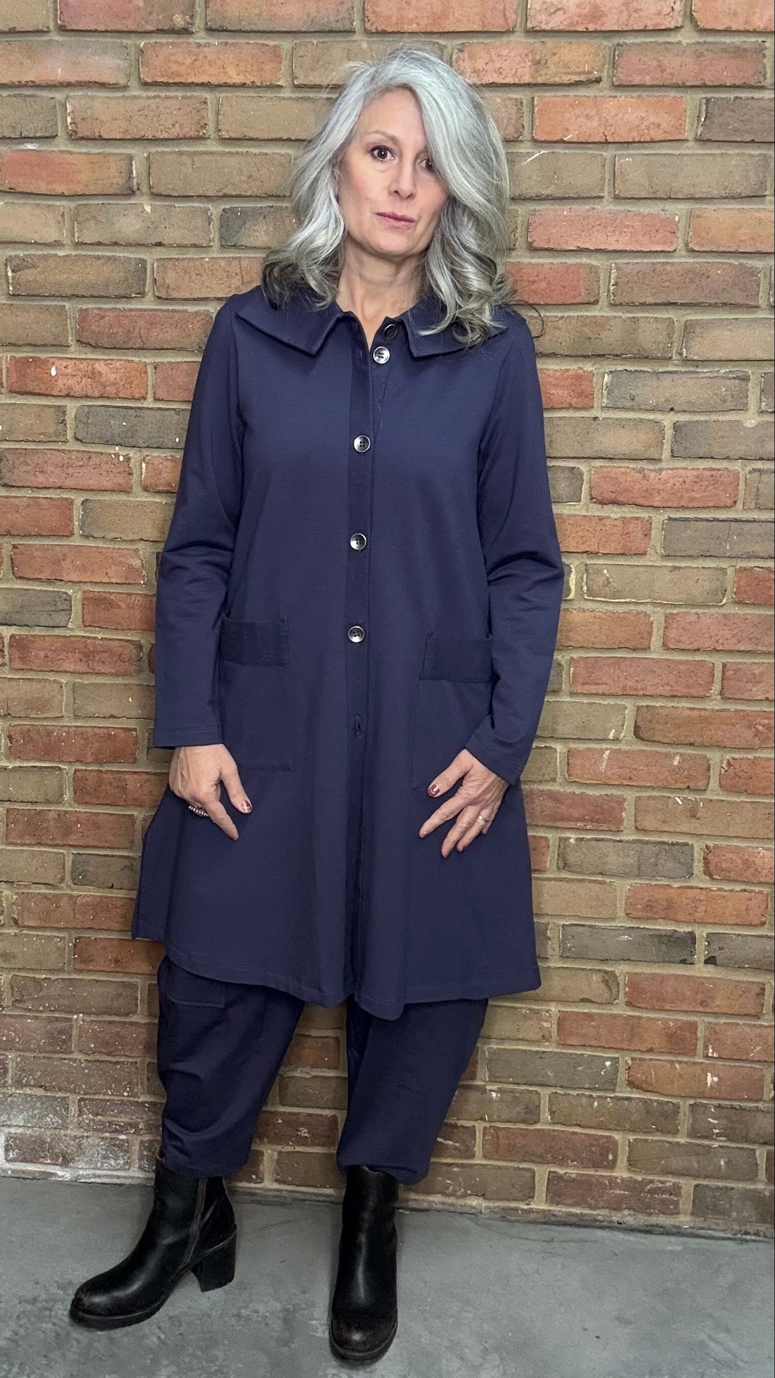 Woman wearing a plum outfit standing against a brick wall.