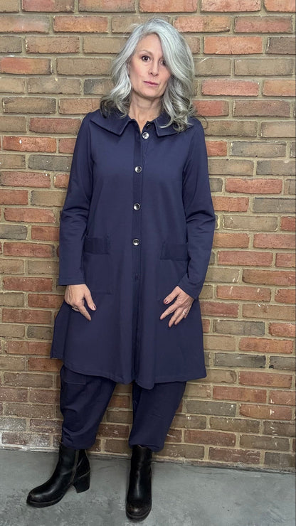 Woman wearing a plum outfit standing against a brick wall.