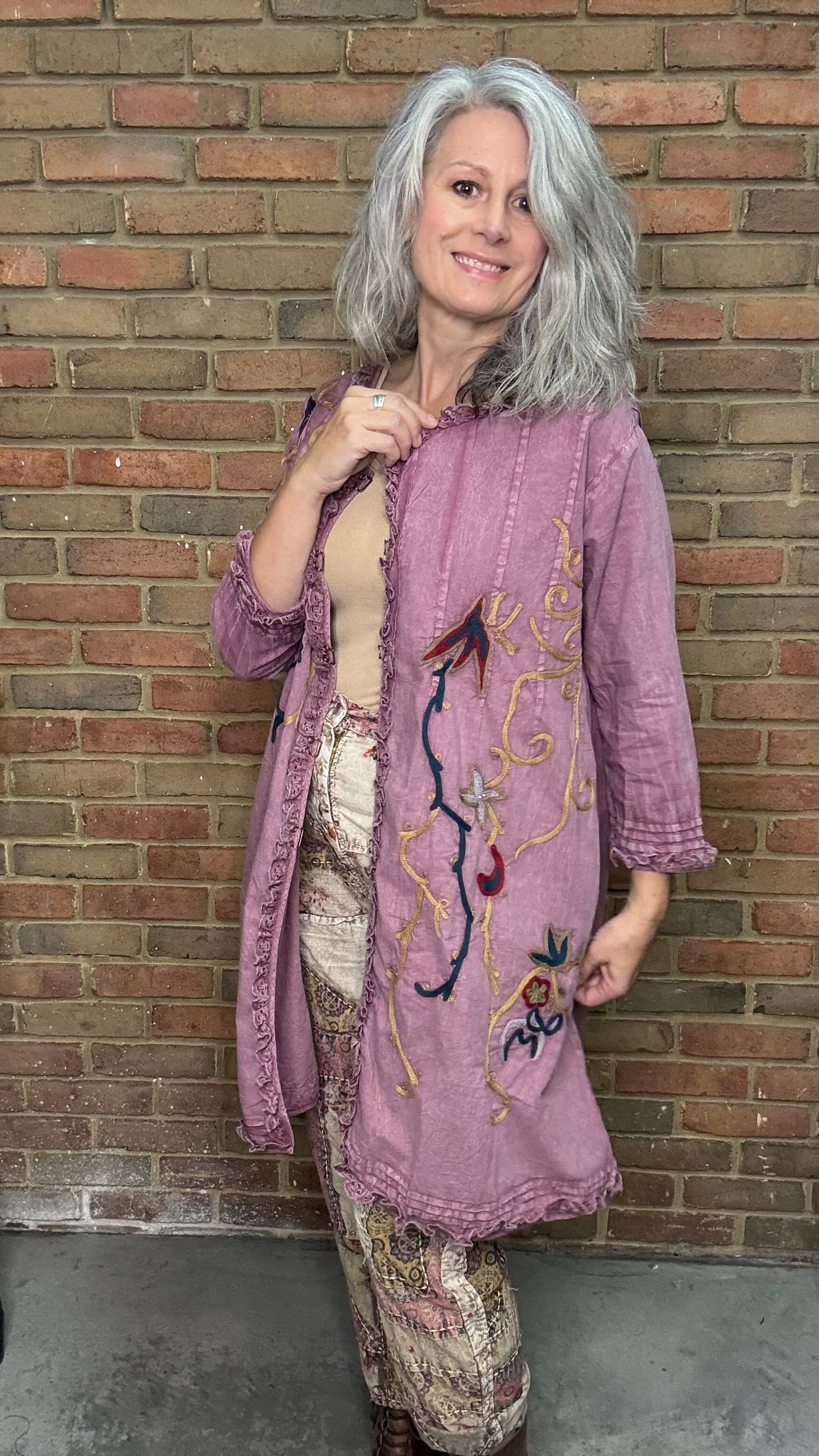 Woman wearing an embroidered pink jacket against a brick wall
