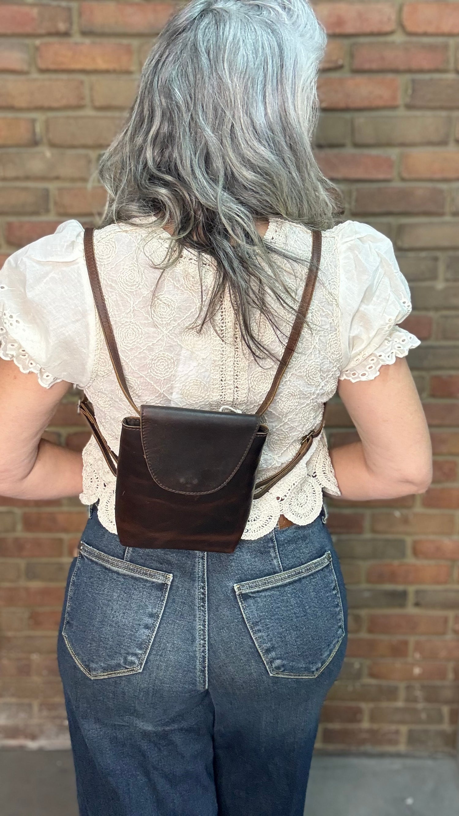 Woman holding a Backpack style leather Handbag with a brick wall in background.