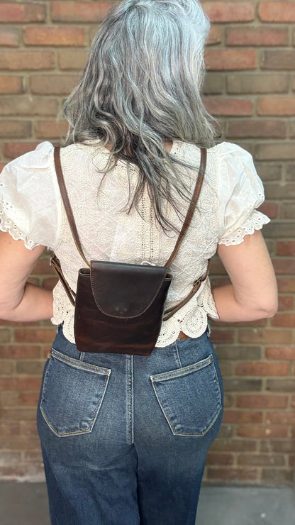 Woman holding a Backpack style leather Handbag with a brick wall in background.