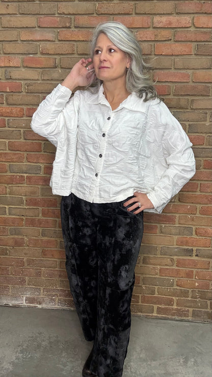 Person wearing a white textured shirt and black pants against a brick wall.