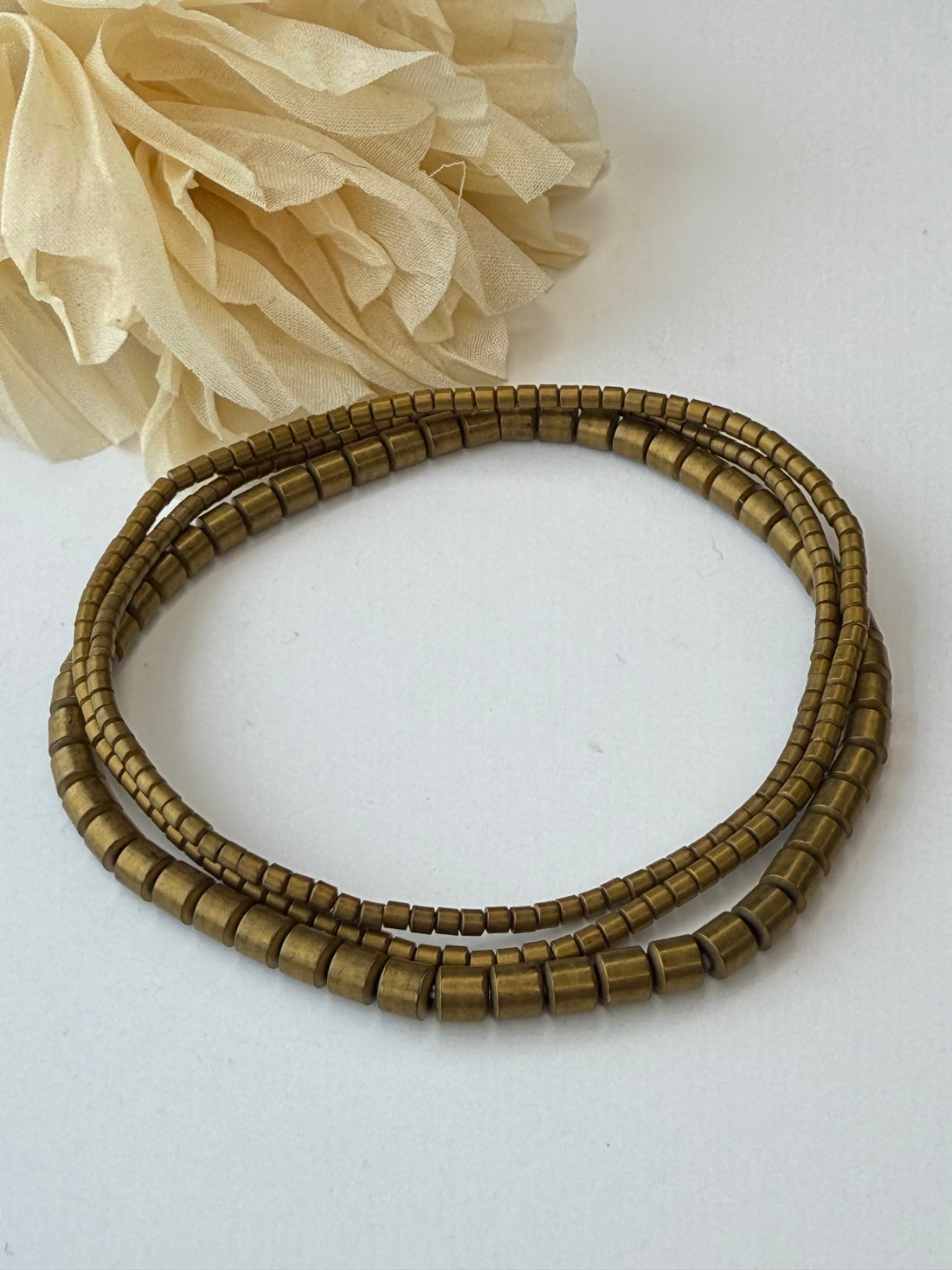 Brass beaded bracelet on a white background with beige fabric