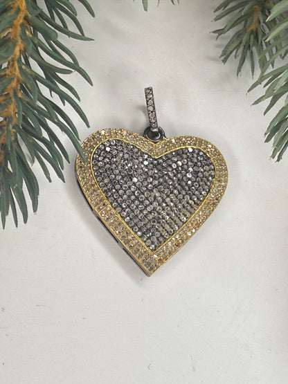 Heart-shaped pendant with gold border and black center all filled with pave diamonds on a light background with greenery.