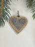 Heart-shaped pendant with gold border and black center all filled with pave diamonds on a light background with greenery.