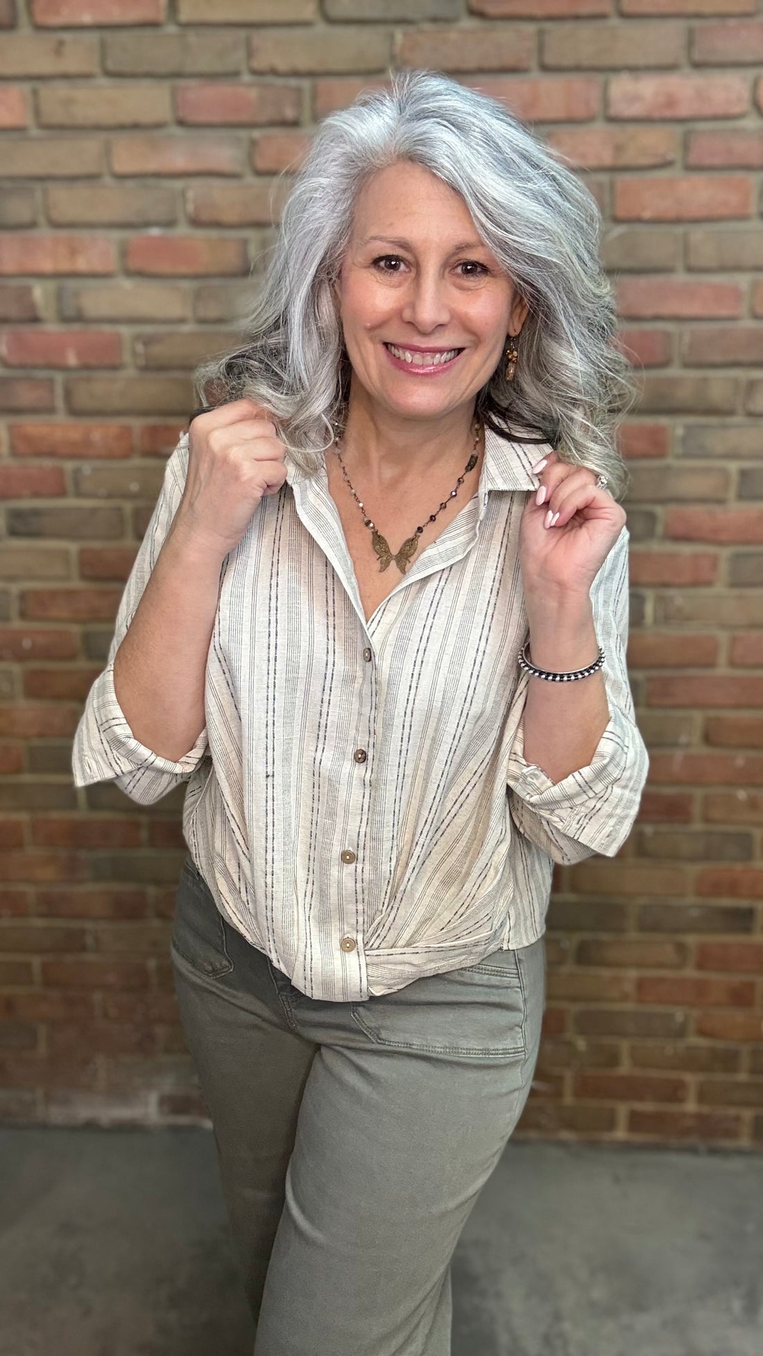 Woman wearing Yarn Dye Stripe Twist Shirt with pants against brick wall.
