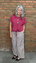 Woman wearing Scalloped Sleeve Tie Hem Top - Berry and striped pants standing against a brick wall.