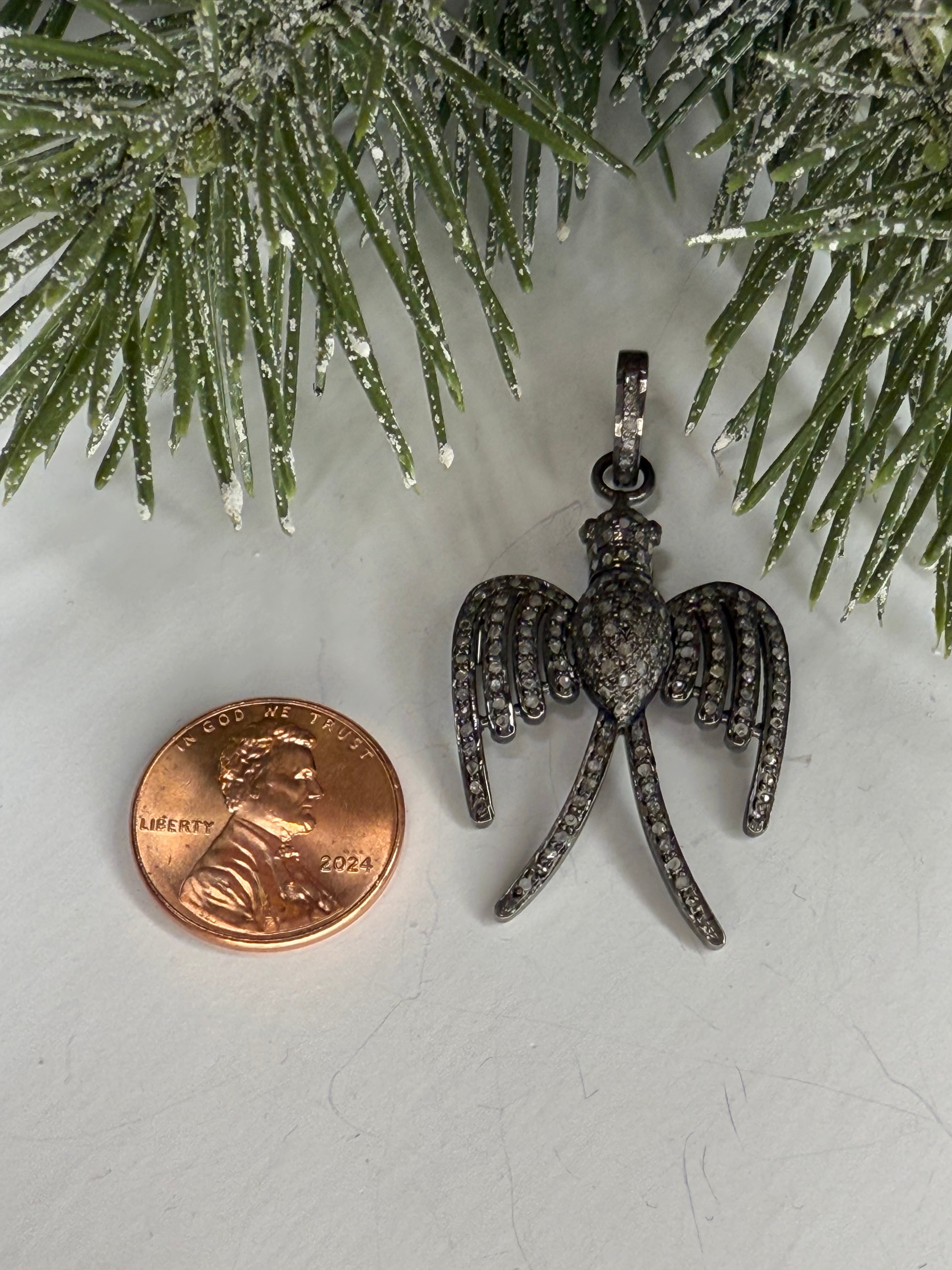 Bird shaped pendant with a penny for scale on a white background with greenery.