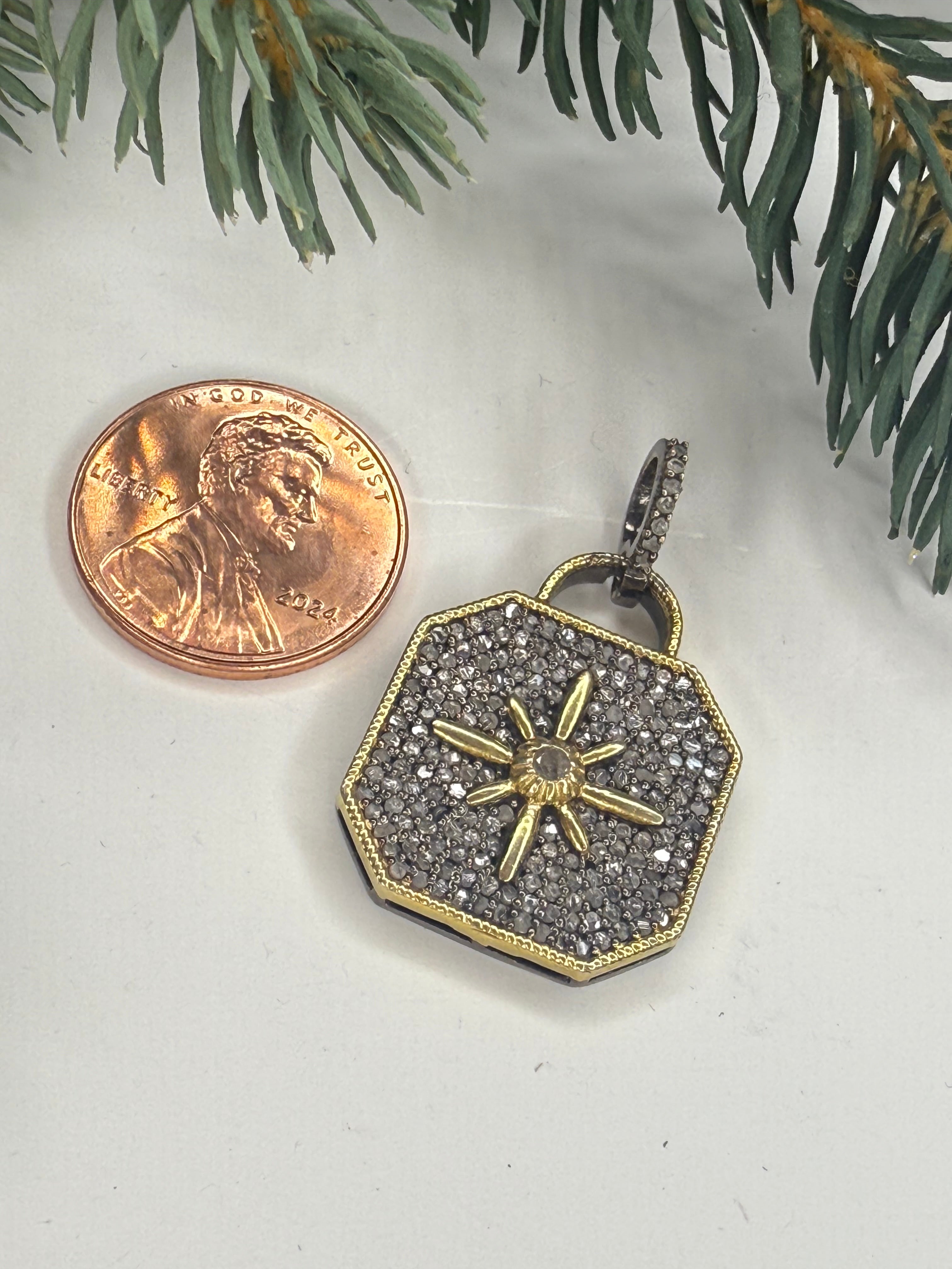Lock shaped pendant with star design next to a penny on a white surface with green leaves.