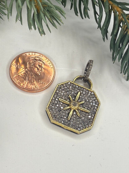 Lock shaped pendant with star design next to a penny on a white surface with green leaves.