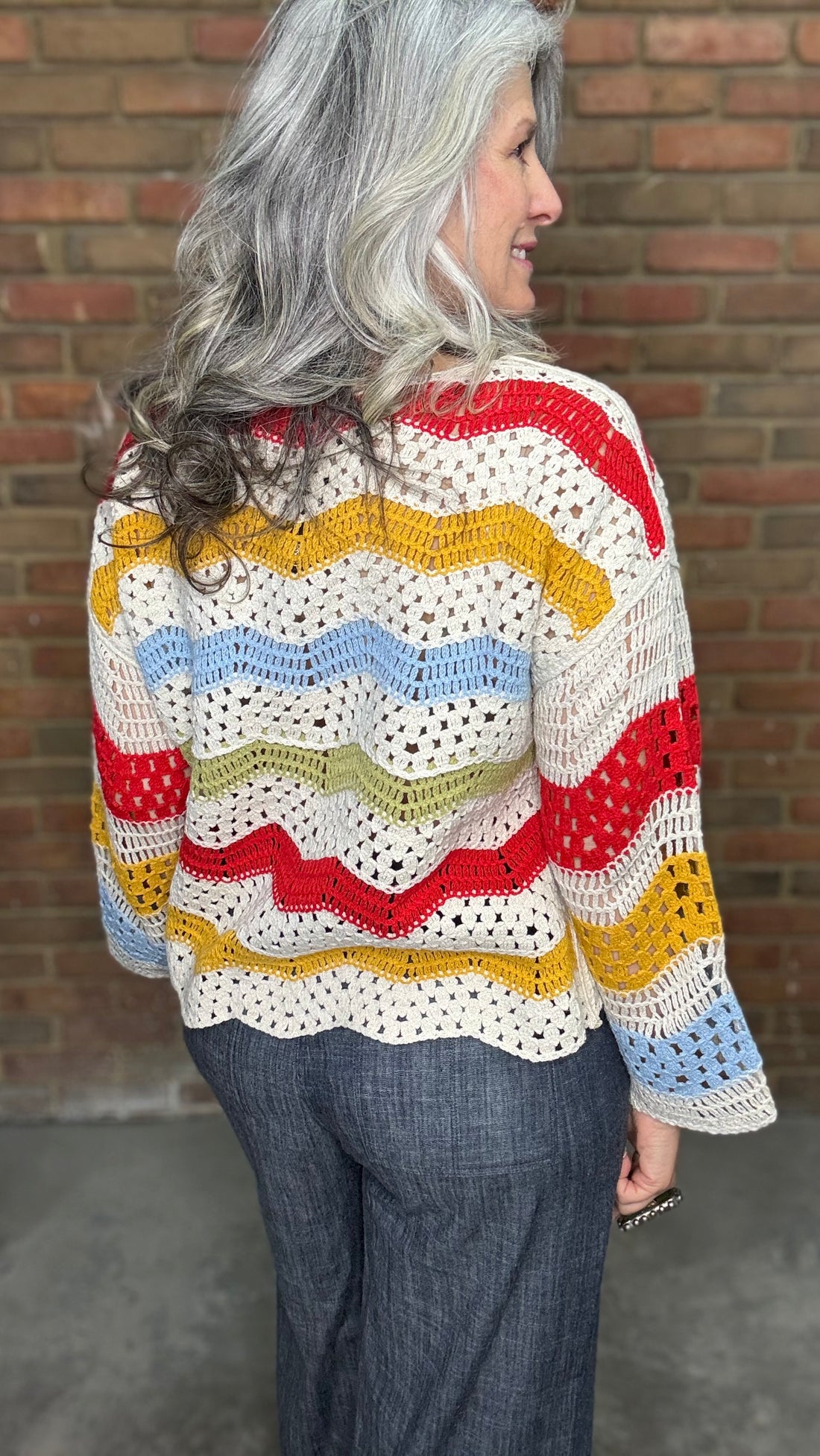 Woman wearing the Sunshine 3/4 Sleeve Crochet Top, a colorful crochet sweater in front of a brick wall.