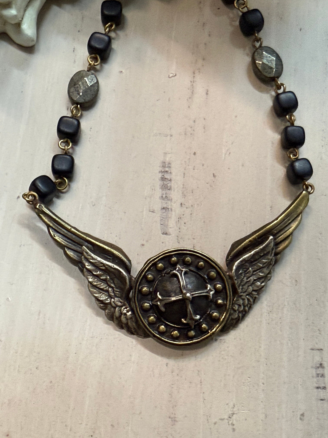Necklace with winged design and black beads on a textured surface
