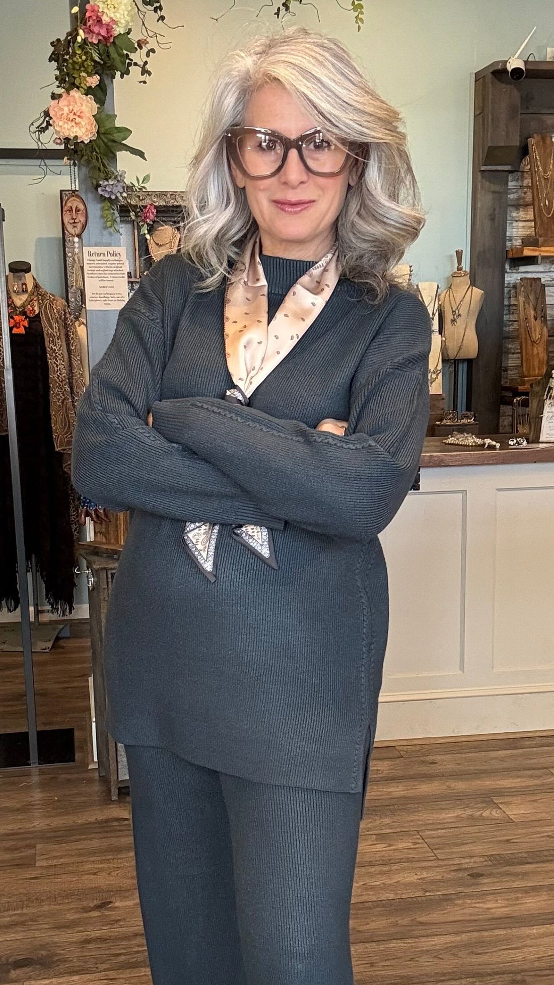 Woman in a denim color sweater set standing in a store with clothing racks and displays.