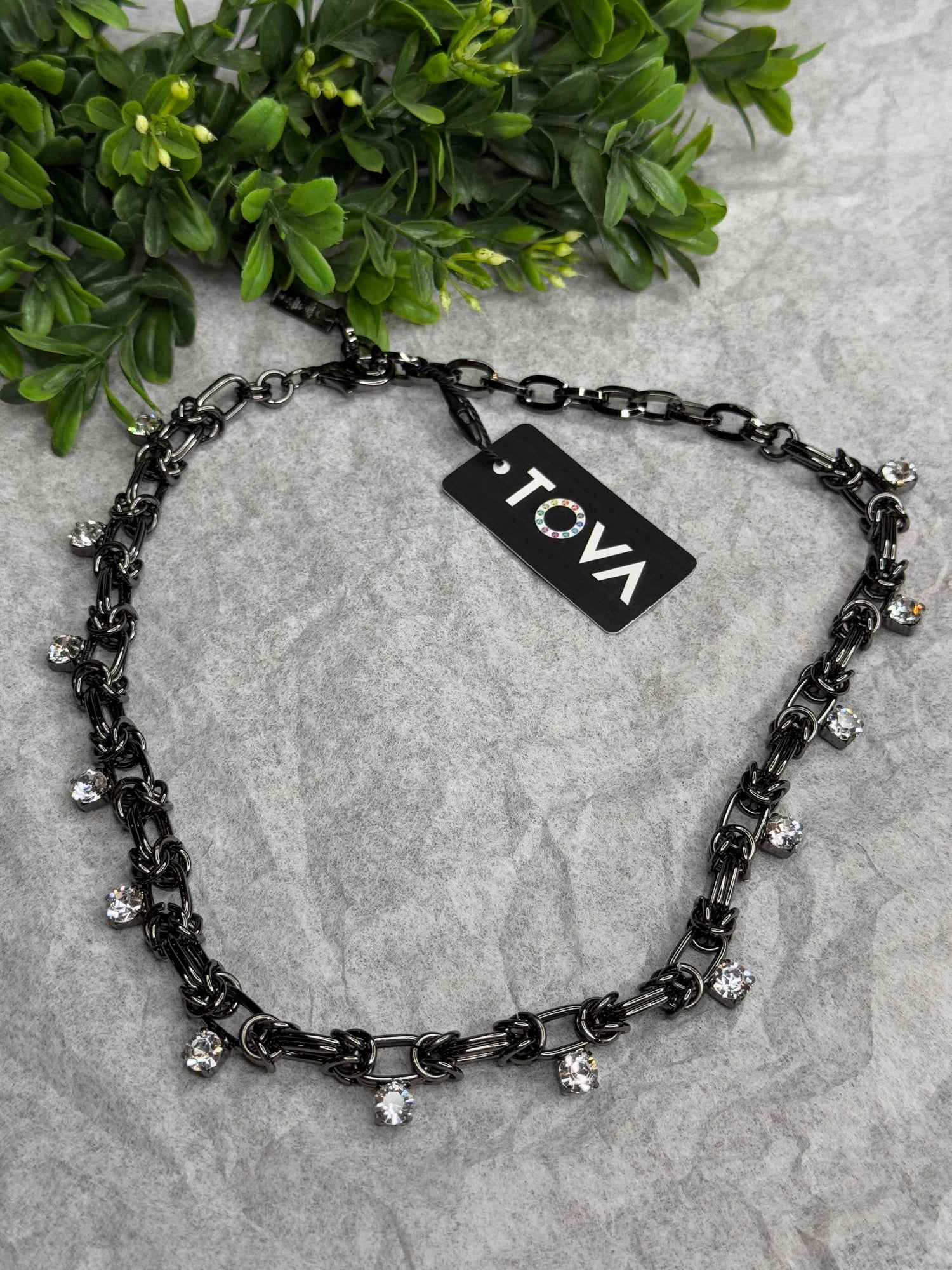 Black chain necklace with decorative elements on a gray surface, featuring a &