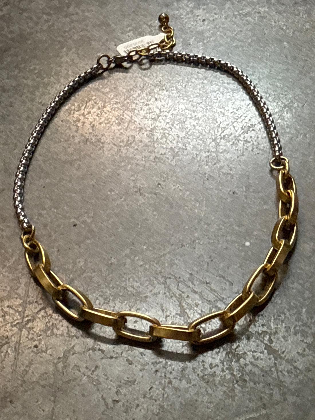 Gold and silver chain necklace on a concrete surface
