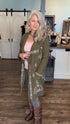 A woman with gray hair stands in a boutique wearing an olive green embroidered cardigan over a pink top, gray pants, and brown boots.