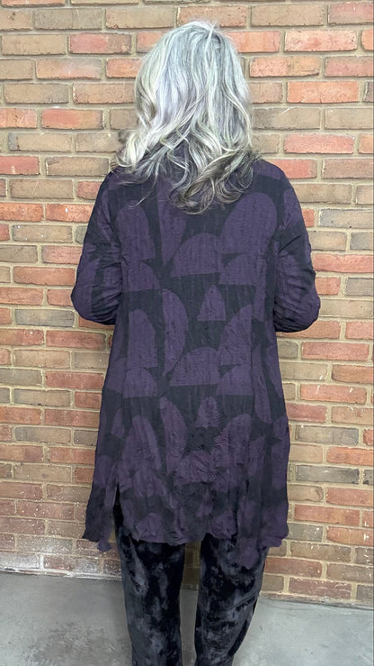 Person wearing a dark patterned outfit standing against a brick wall.