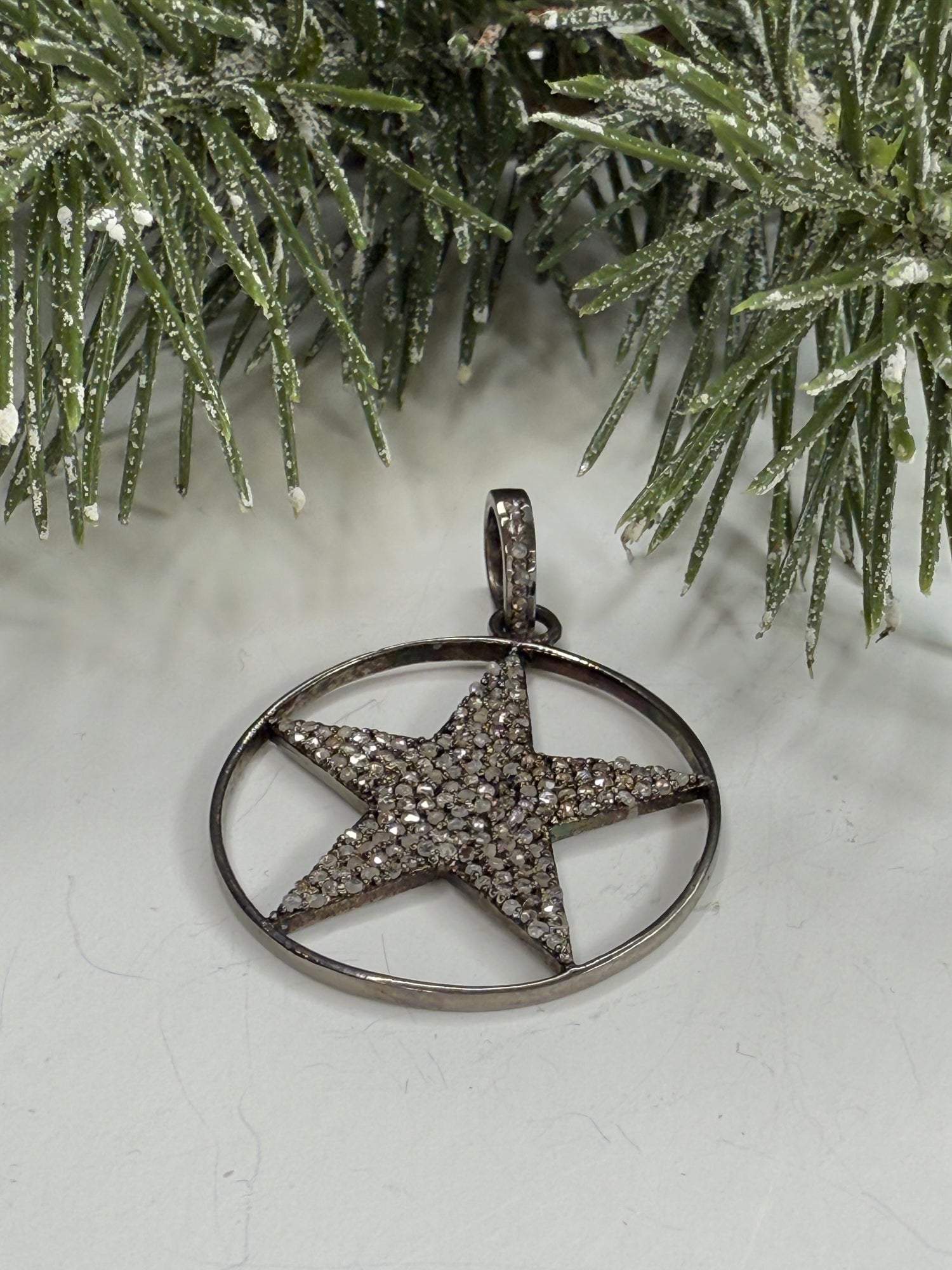 Lone star pendant with pave diamonds on a white surface with a Christmas tree branch.