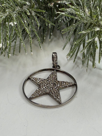 Lone star pendant with pave diamonds on a white surface with a Christmas tree branch.